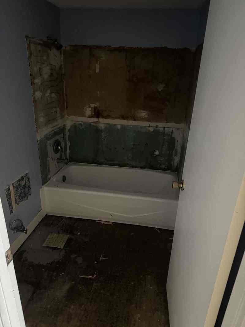 A bathroom mid-demolition with the tub removed and exposed wall framing.